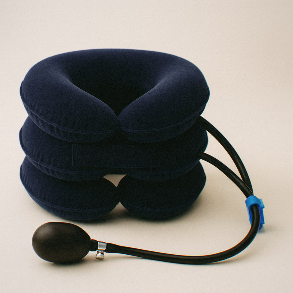Navy inflatable neck traction collar seen from the front on a cream background, with its tube, blue clamp and hand pump
